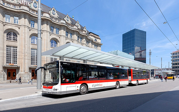 Un bus avec remorque des transports urbains saint-gallois sous un avant-toit devant la gare.